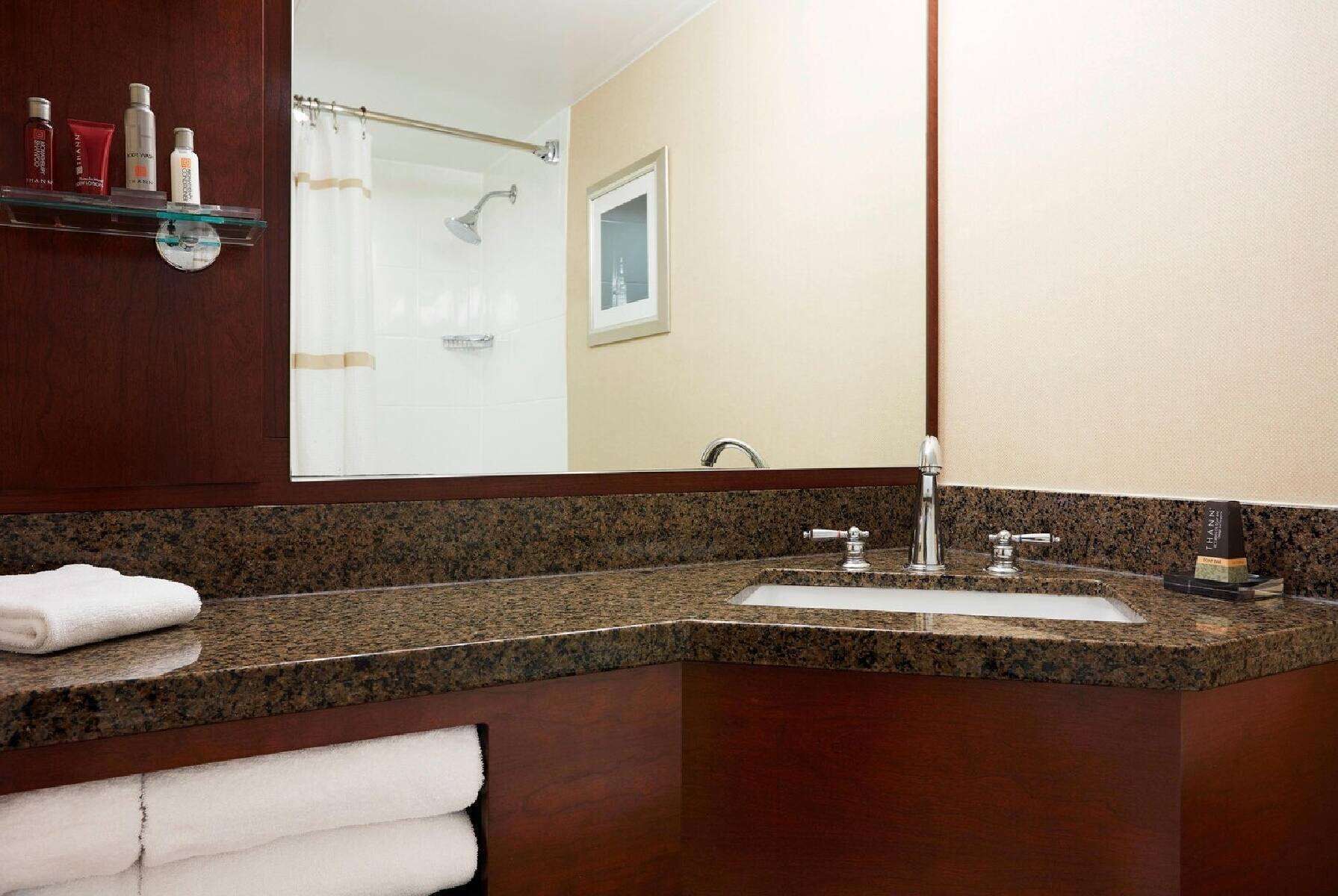 A bathroom with a granite countertop, a sink, and a mirror. There are towels and toiletries on a shelf.