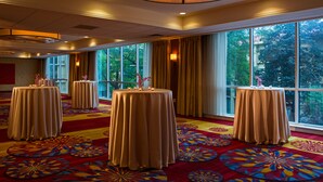A hotel room with large windows, a red carpet, and four round tables with candles.