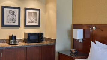 A hotel room with a kitchenette, a bed, and two framed pictures on the wall.