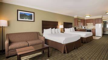 A hotel room with two beds, a sofa, a small table, a kitchen area, and a framed picture on the wall.