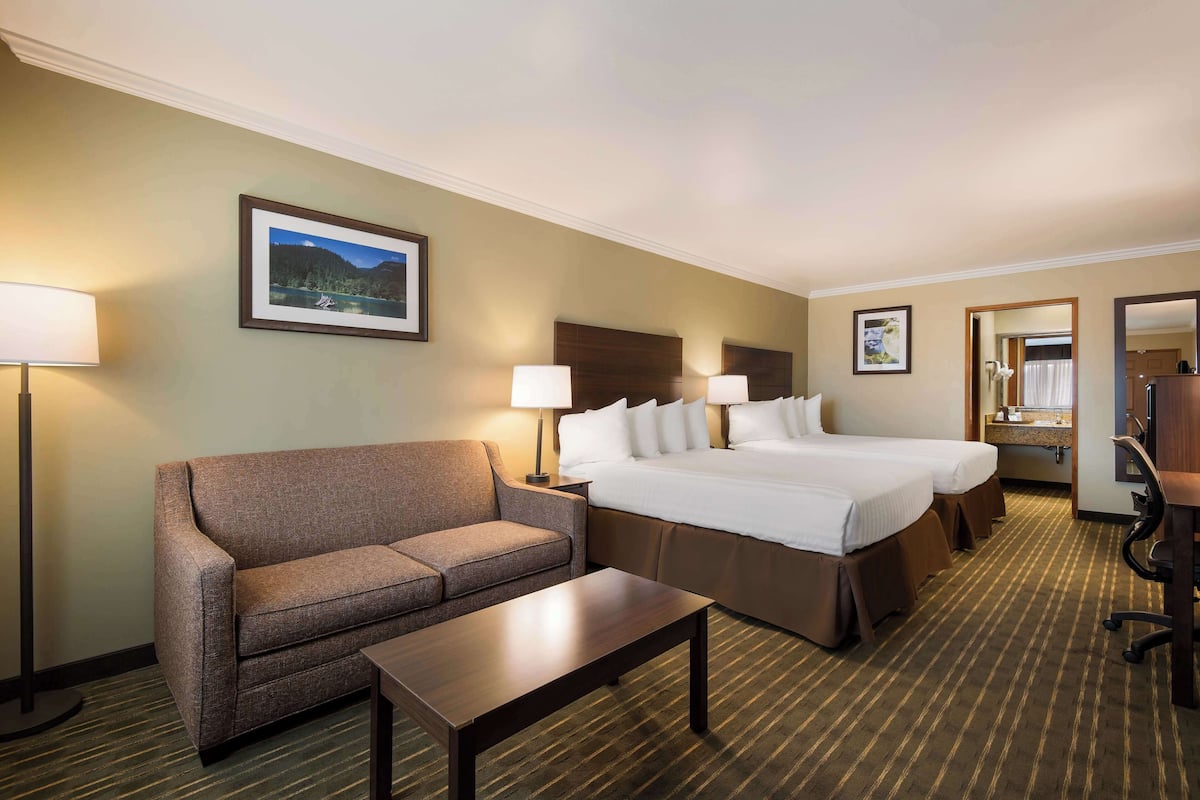 A hotel room with a sofa, two single beds, a desk, and a lamp.