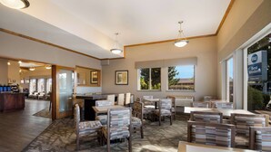 A hotel lobby with a dining area, wooden flooring, and large windows offering views. - Best Western Holiday Hotel (Coos Bay)