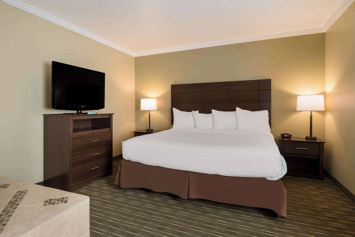 A hotel room with a large bed, a flat-screen TV, two bedside lamps, and a wooden dresser.