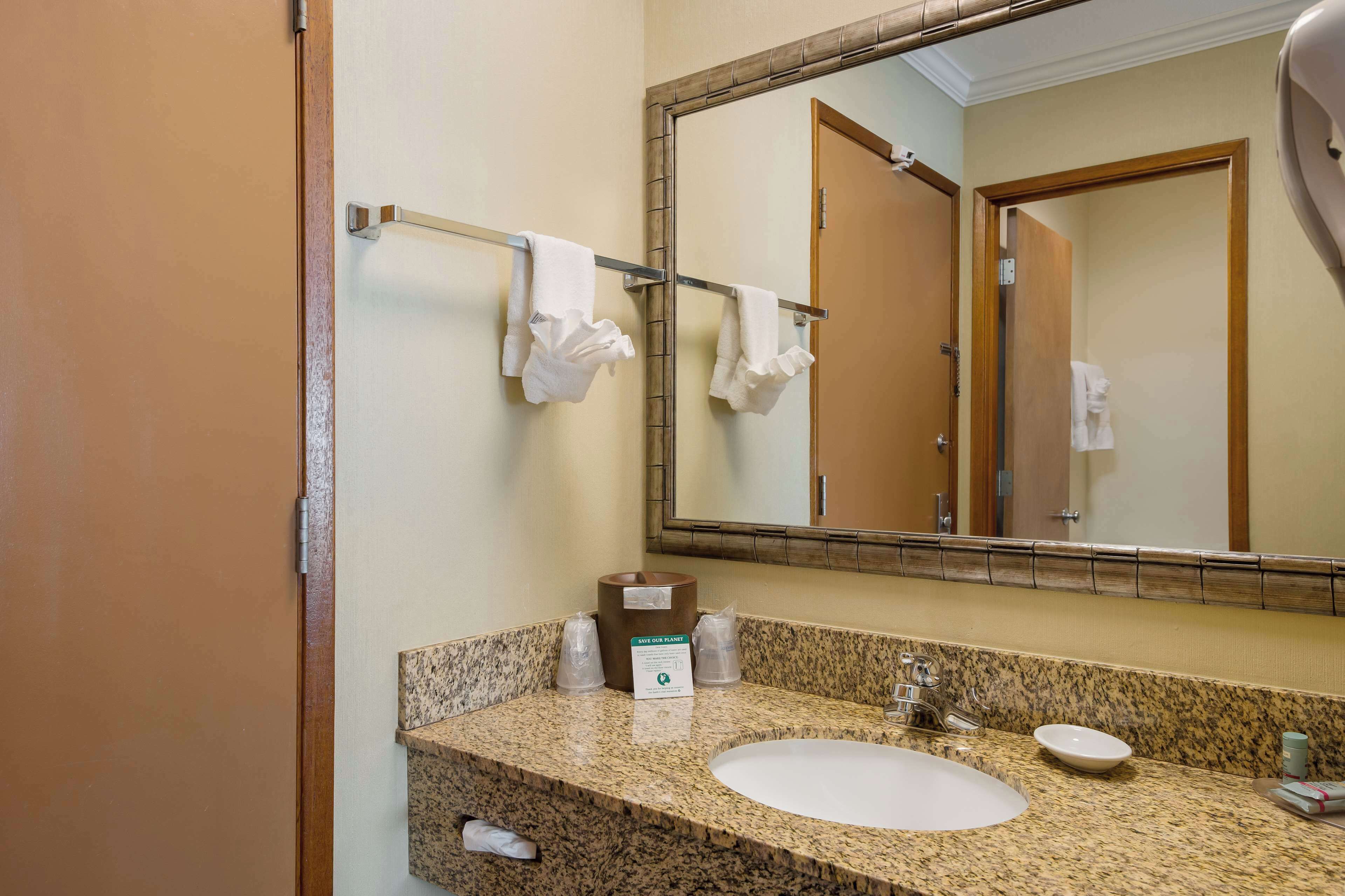 A bathroom with a granite countertop, a white sink, a mirror, and a towel rack with a white towel.