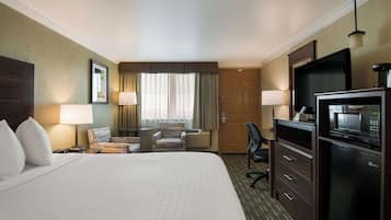 A hotel room with a large bed, a desk with a chair, a television, a microwave, and a minibar.