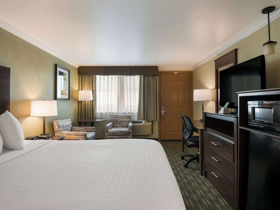 A hotel room with a large bed, a desk with a chair, a television, a microwave, and a minibar.