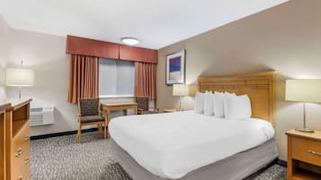 Een hotelkamer met een groot bed, twee stoelen, een bureau, een lamp en een raam met gordijnen.