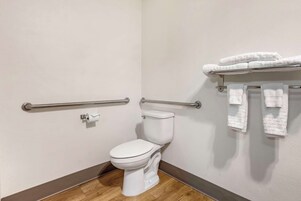 Un baño moderno con inodoro blanco, barras de apoyo y toallero.