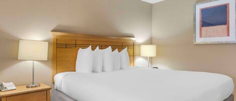 A hotel room with a large bed, wooden headboard, two bedside lamps, a nightstand with a phone, and a framed picture on the wall.
