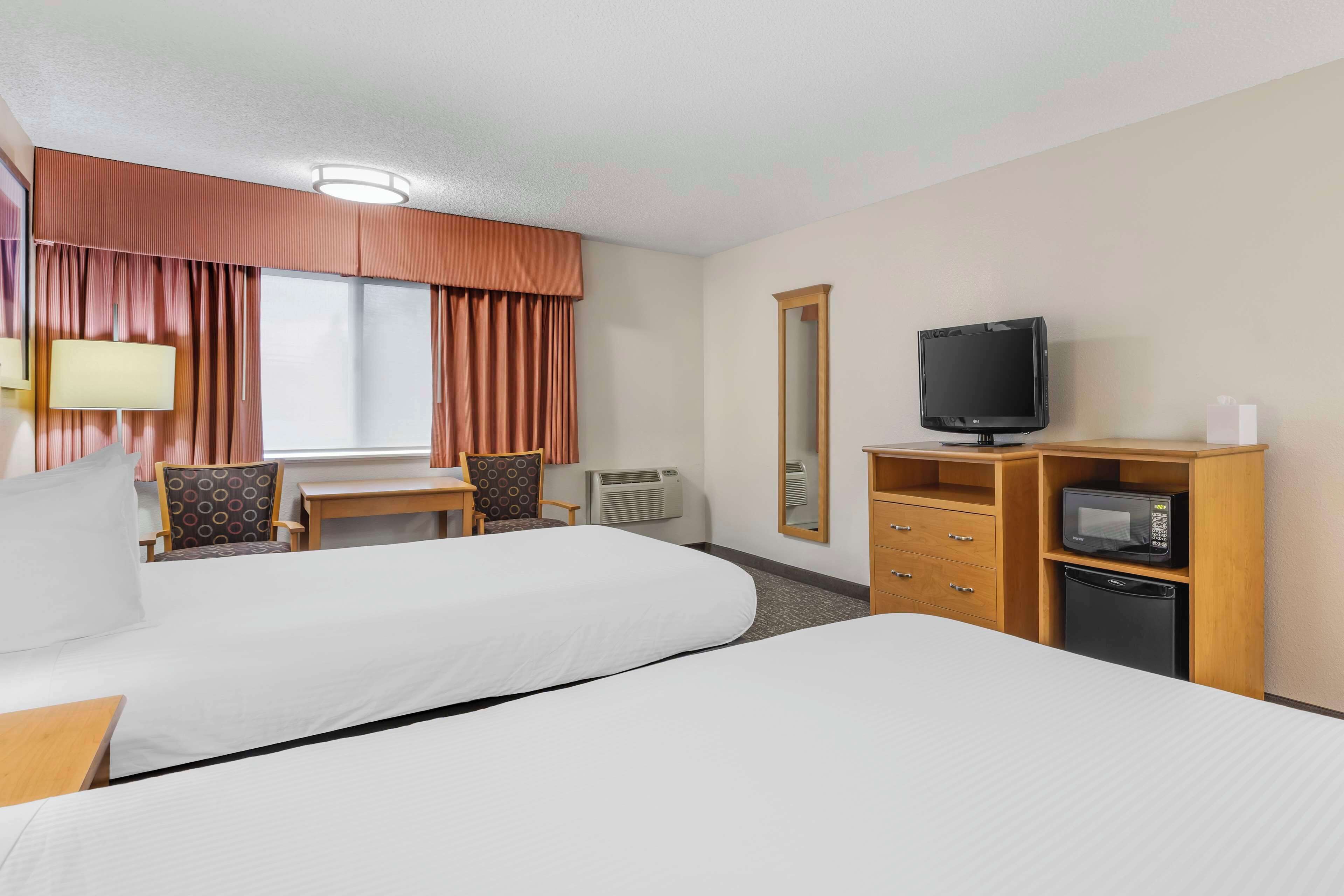 A hotel room with two beds, a desk with a chair, a television, a microwave, and a small refrigerator.