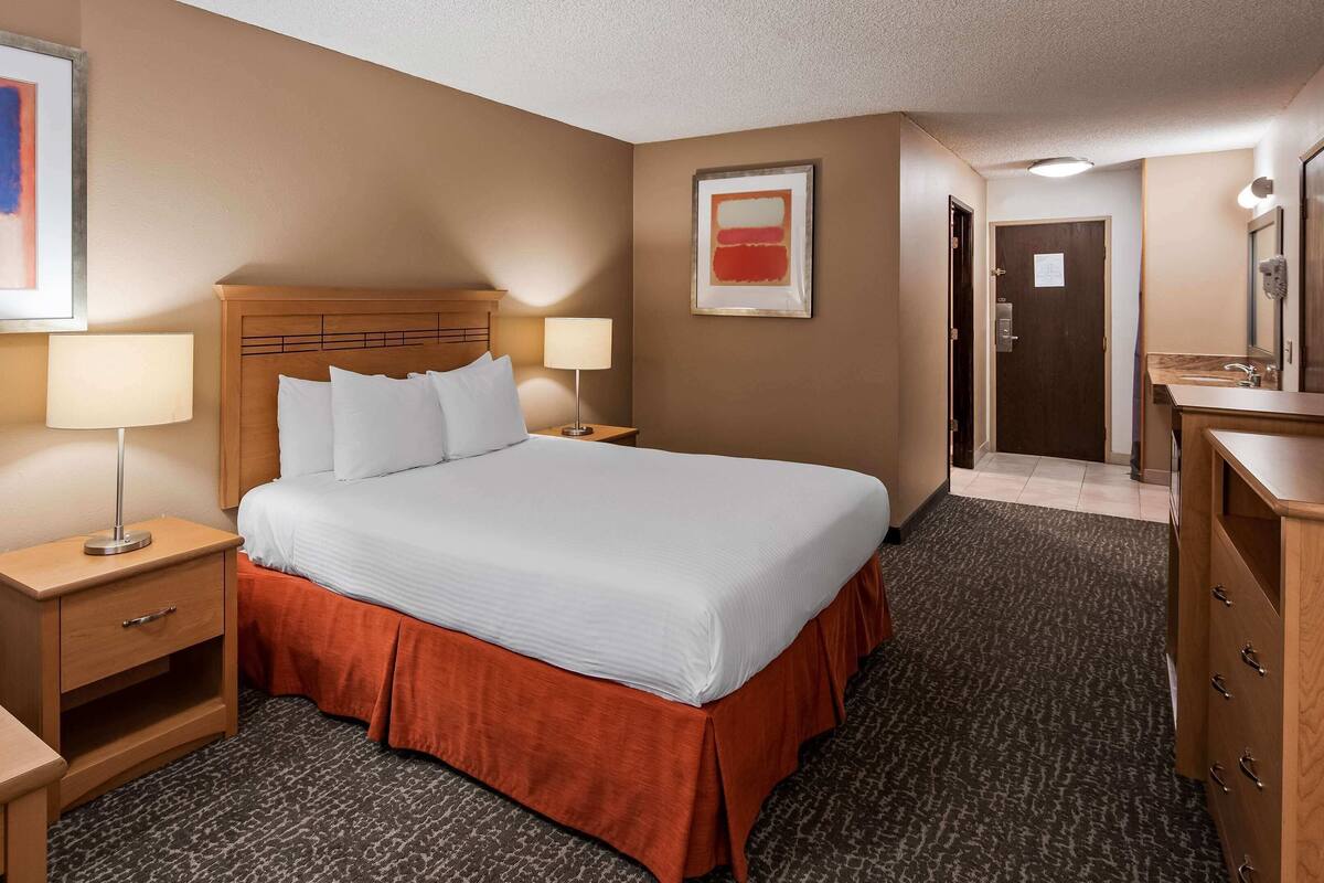 Ein Hotelzimmer mit Bett, Nachttischen, Schreibtisch, Fernseher und einer Badezimmertür.