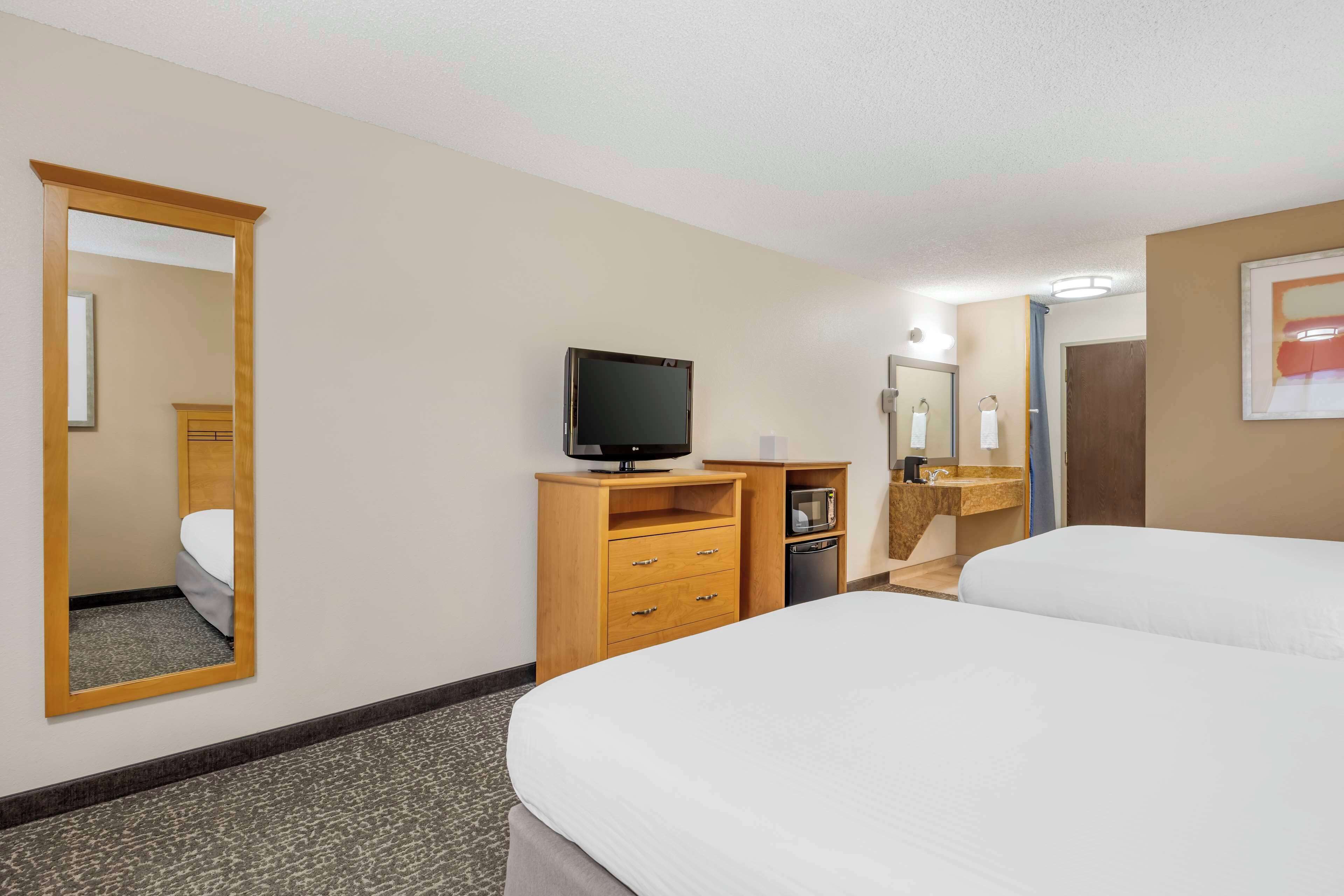 Ein Hotelzimmer mit einem Bett, einem Fernseher auf einem Holzständer, einem kleinen Schreibtisch mit einer Mikrowelle und einem Spiegel an der Wand.