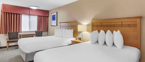A hotel room with two beds, a desk, a chair, a lamp, and a window with curtains.