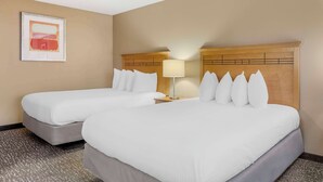 Habitació d'hotel amb dos llits, un capçal de llit de fusta, una tauleta de nit amb una làmpada i un quadre amb marc a la paret.