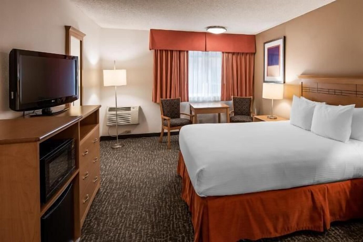 A hotel room with a bed, a desk, a chair, a television, and a lamp.