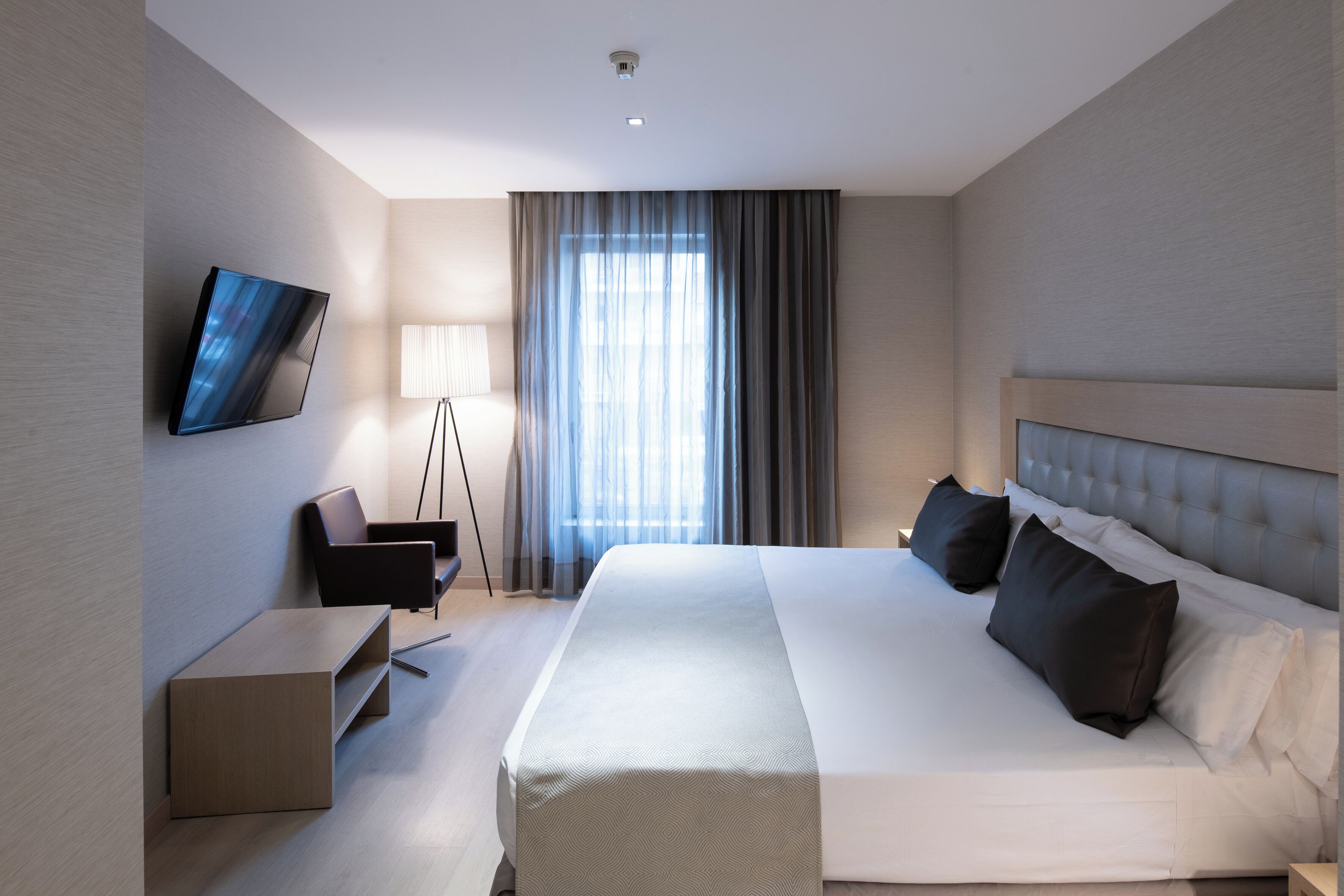 Habitación de hotel moderna con una cama grande, un televisor de pantalla plana en la pared, un escritorio y una lámpara de pie.