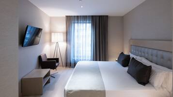 Habitación de hotel moderna con una cama grande, un televisor de pantalla plana en la pared, un escritorio y una lámpara de pie.