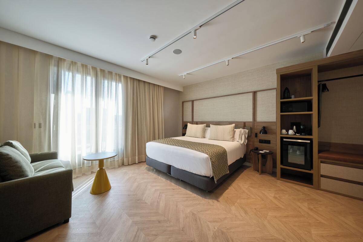 Quarto de hotel moderno com uma cama grande, um sofá, uma mesa pequena e um guarda-roupa embutido.