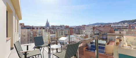 Varanda com duas cadeiras e uma mesa, com vista para um horizonte urbano com edifícios e o topo de uma igreja.