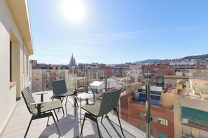 A balcony with two chairs and a table, overlooking a cityscape with buildings and a church spire. - Catalonia Sagrada Familia (Barcelona)