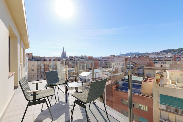 A balcony with two chairs and a table, overlooking a cityscape with buildings and a church spire. - Catalonia Sagrada Familia (Barcelona)