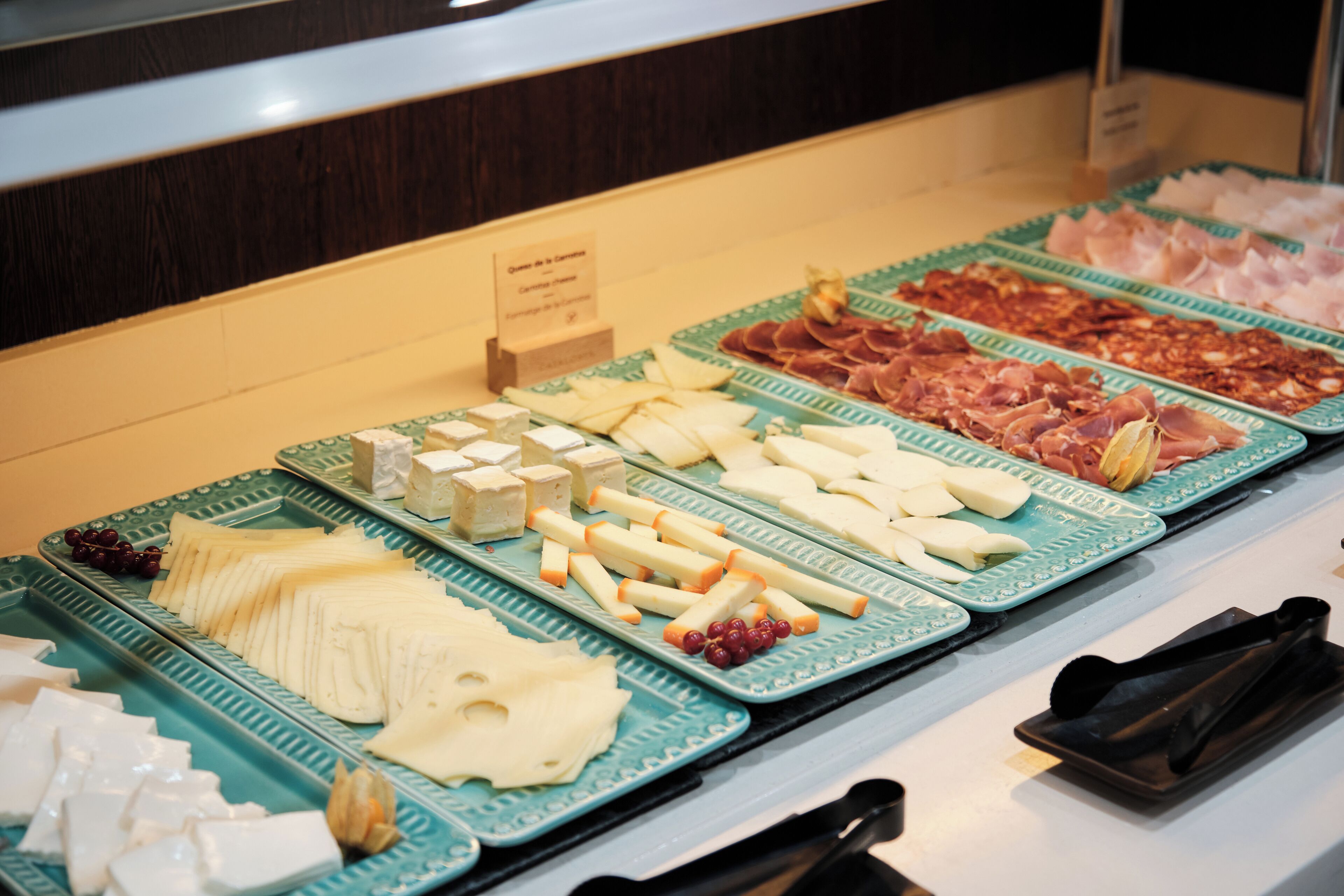 Un bufé con quesos, carnes y frutas variados.