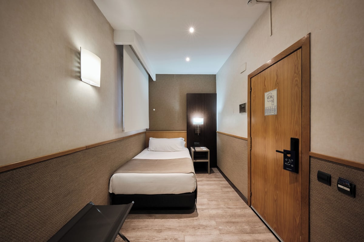 Quarto de hotel com cama, mesa de cabeceira e guarda-roupa de madeira.