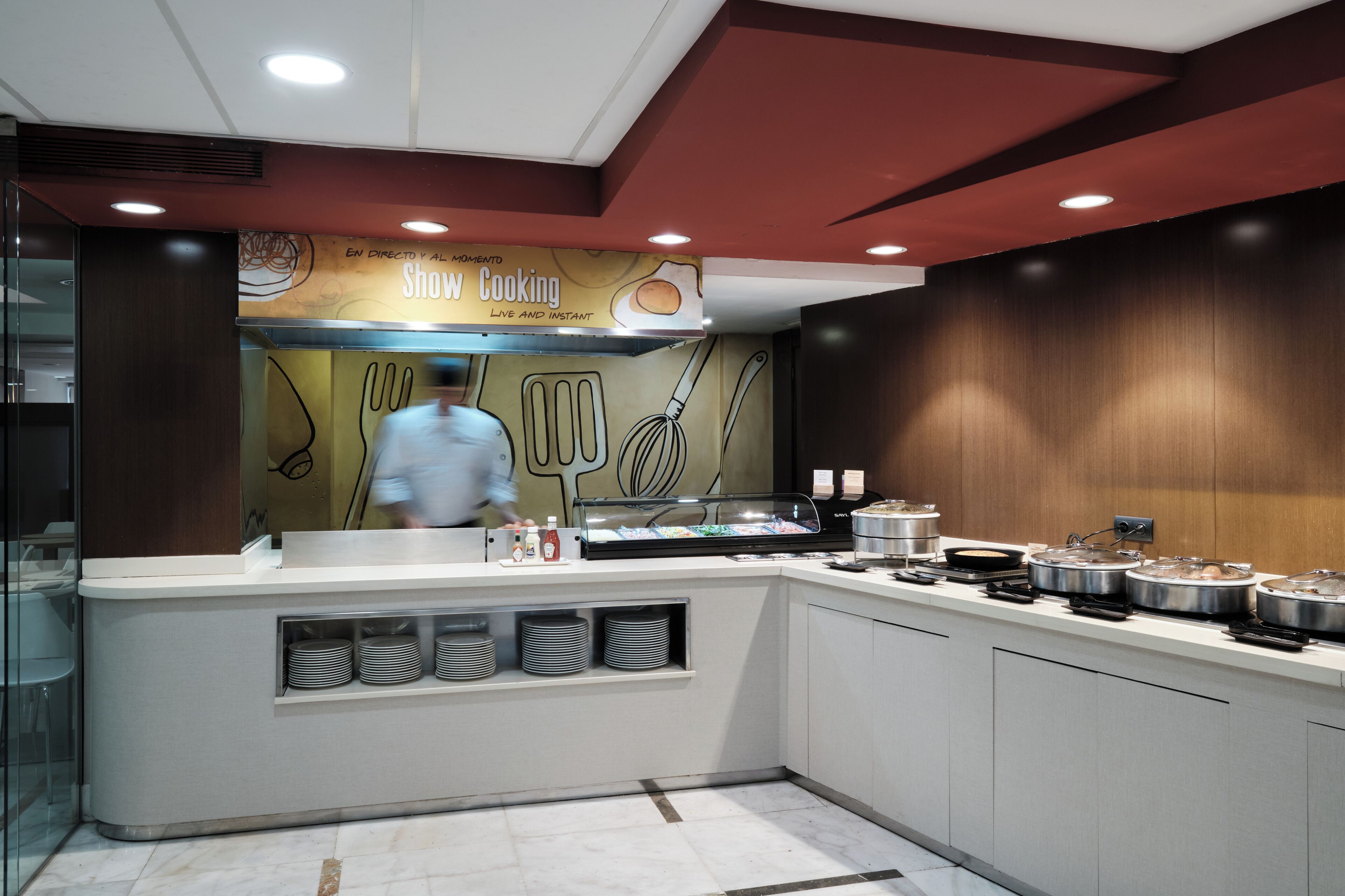 A modern kitchen with a chef preparing food, a display case with utensils, and a counter with cooking equipment.