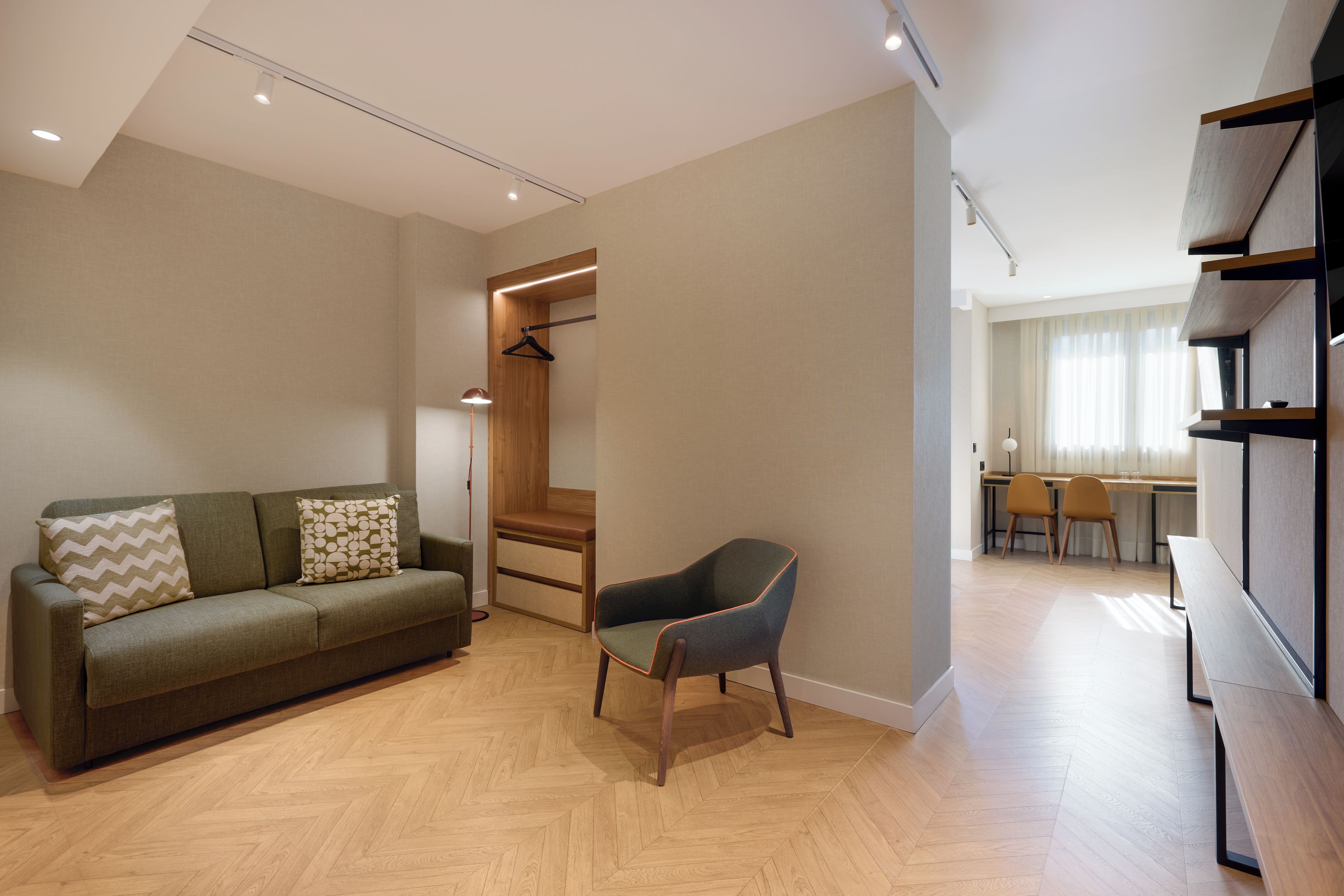 A modern living room with a sofa, a chair, a wooden cabinet, and a desk with chairs.