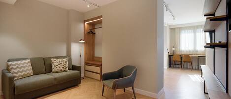 A modern living room with a sofa, a chair, a wooden cabinet, and a desk with chairs.