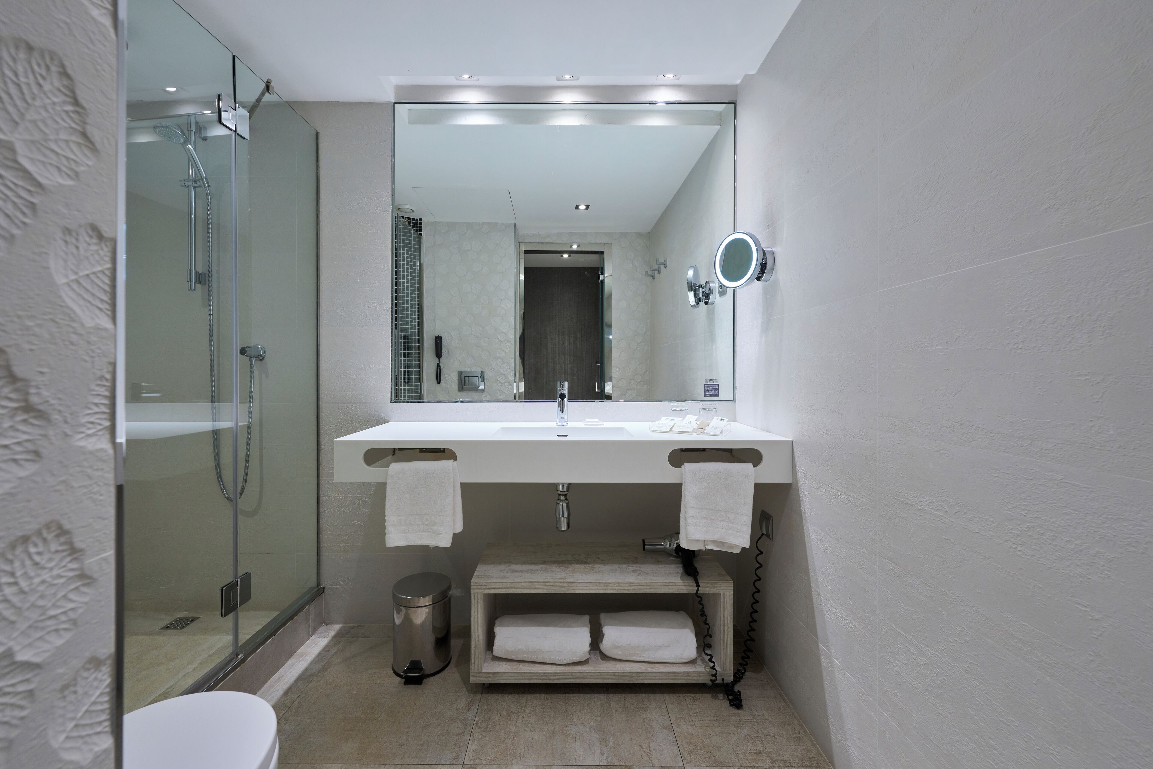 Een moderne badkamer met een glazen douchecabine, een wit wastafelmeubel en een inbouw handdoekhouder.