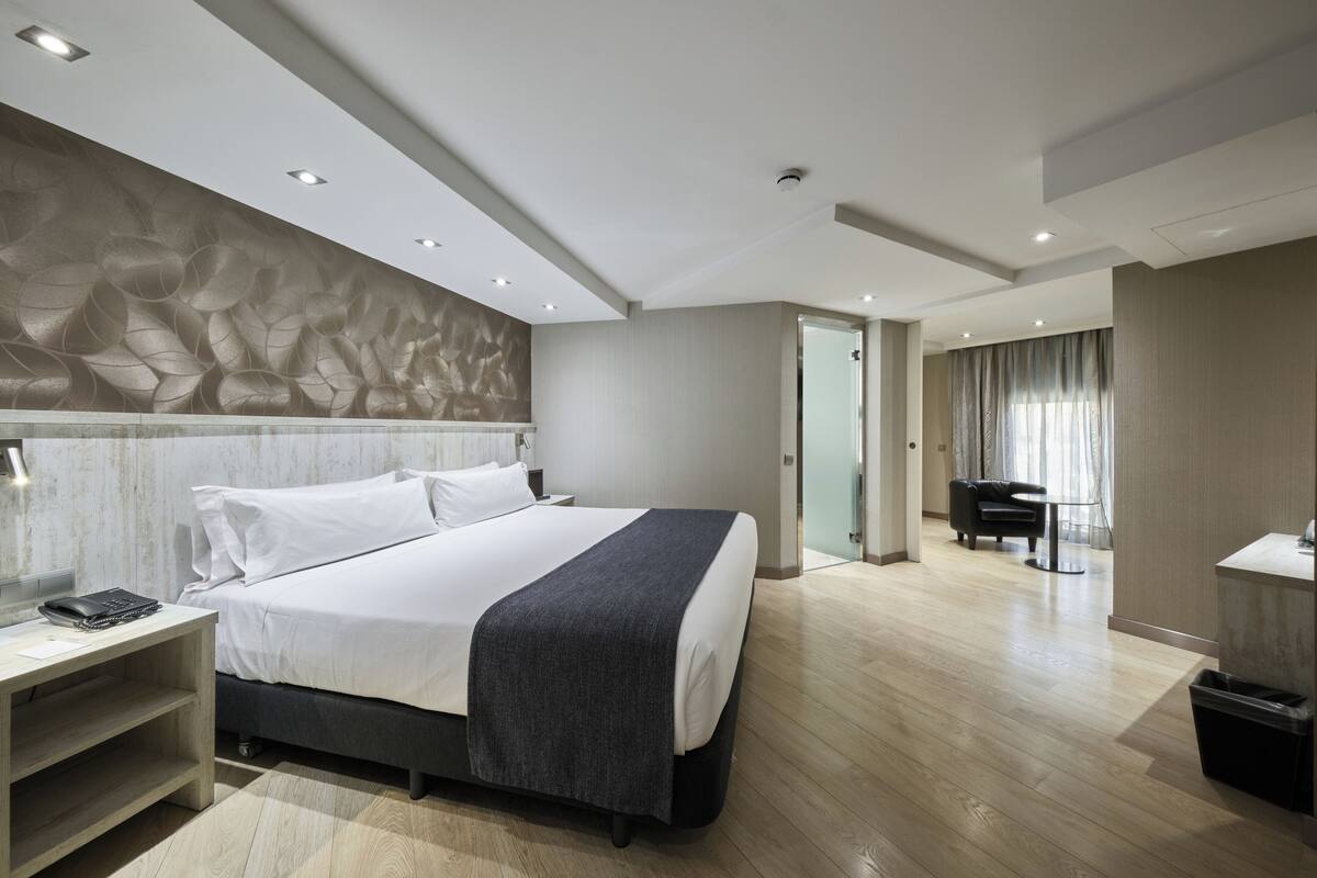 Quarto de hotel moderno com uma cama grande, mesa de cabeceira e área de trabalho.