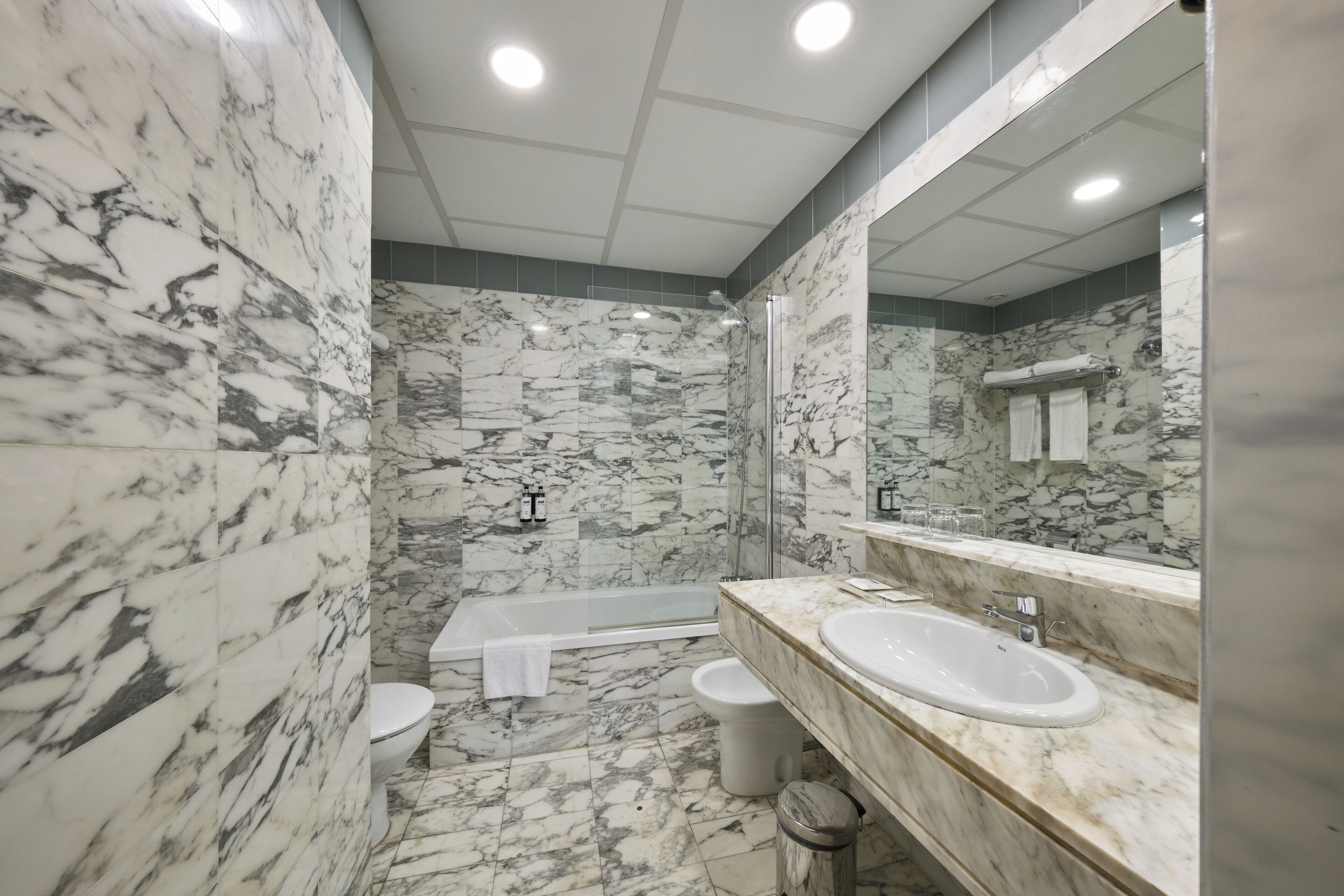 A bathroom with marble walls, a bathtub, a toilet, and a sink.