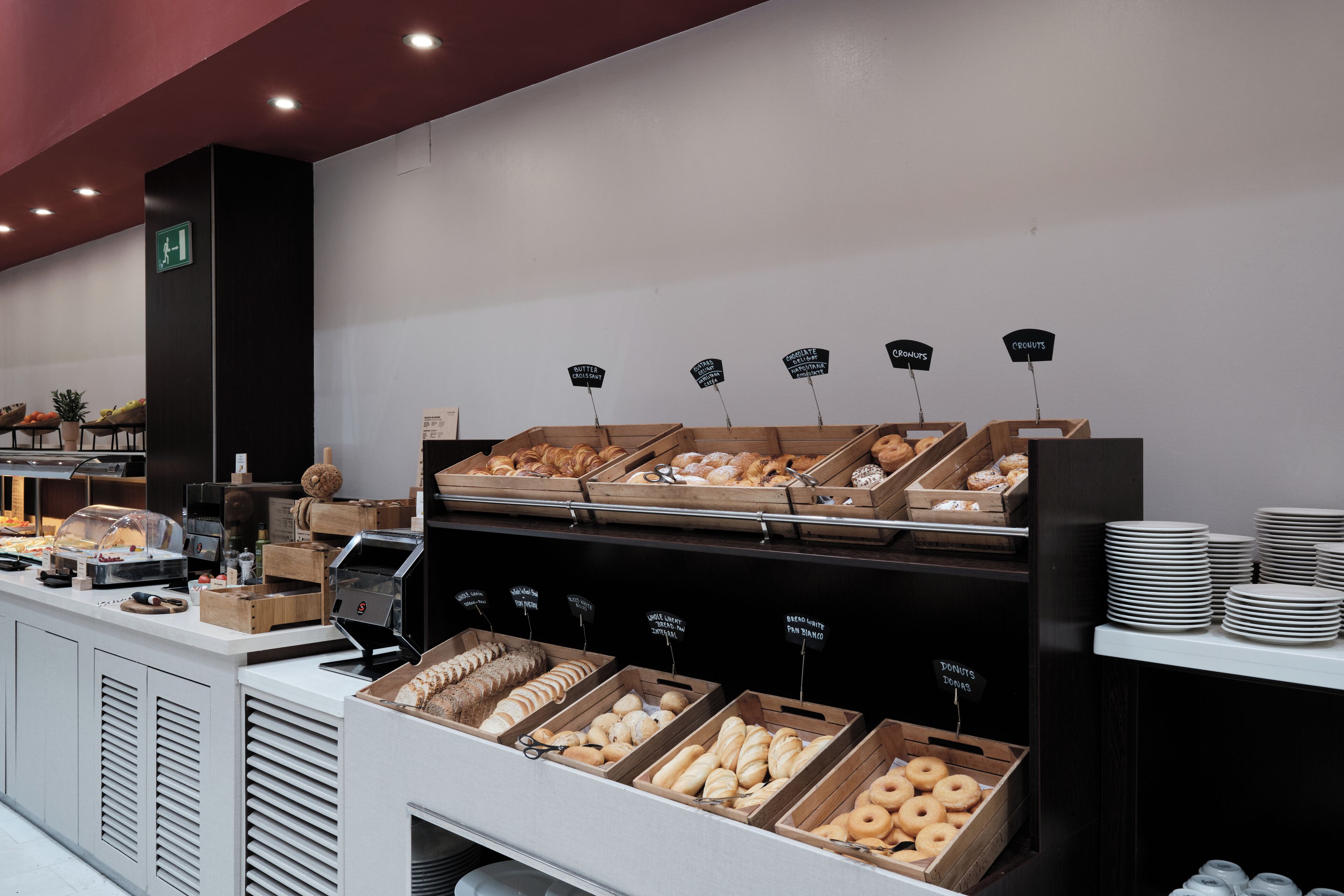 A bakery display with various baked goods in wooden boxes, a coffee machine, and a sign indicating the exit.