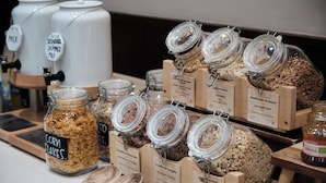 A variety of food items displayed in jars and wooden containers with labels, including corn flakes, chocolate, and other snacks. - Catalonia Sagrada Familia (Barcelona)