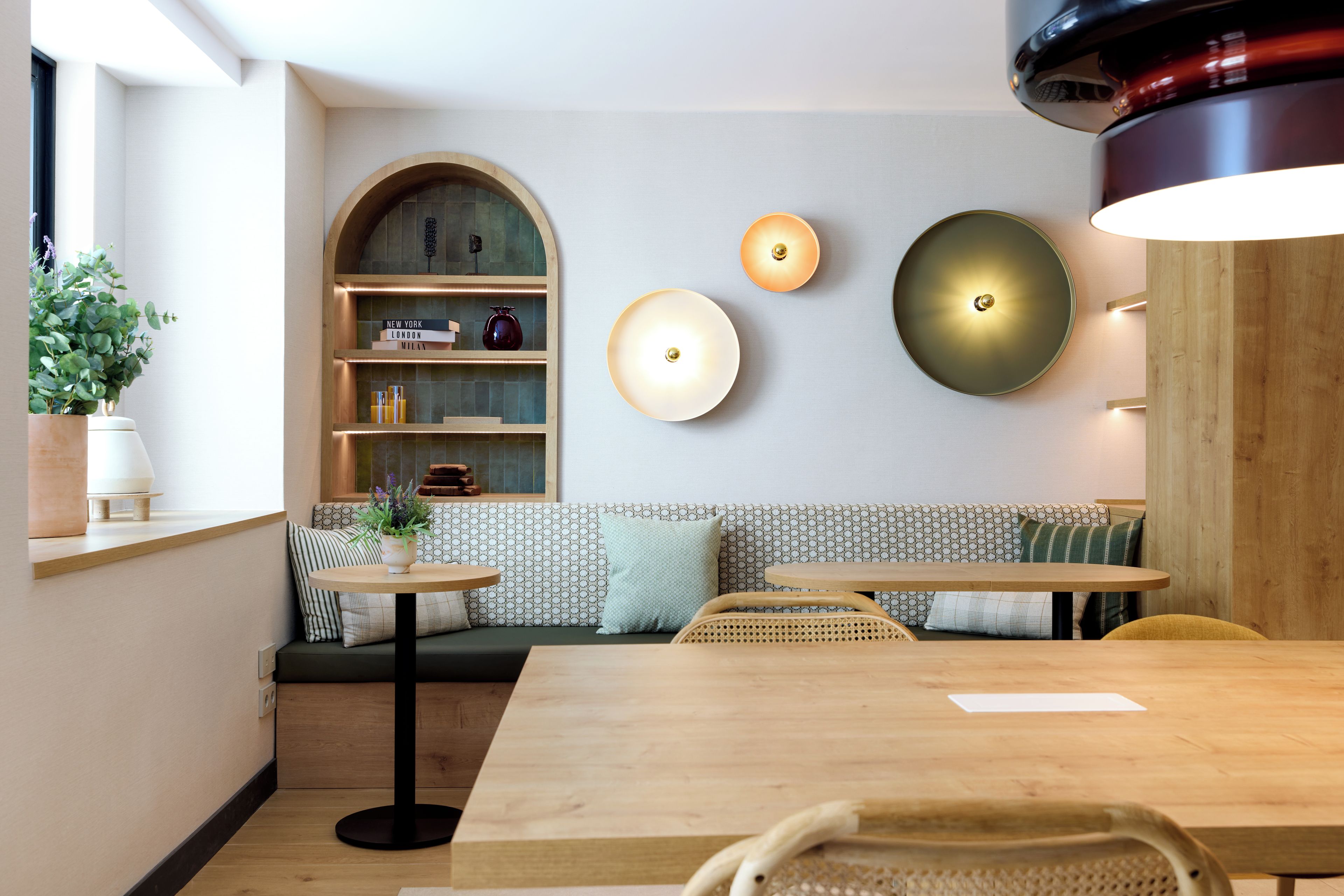 Ein modernes Interieur mit einem Holztisch, einer Bank mit Kissen, einem Bücherregal und Wandleuchten.