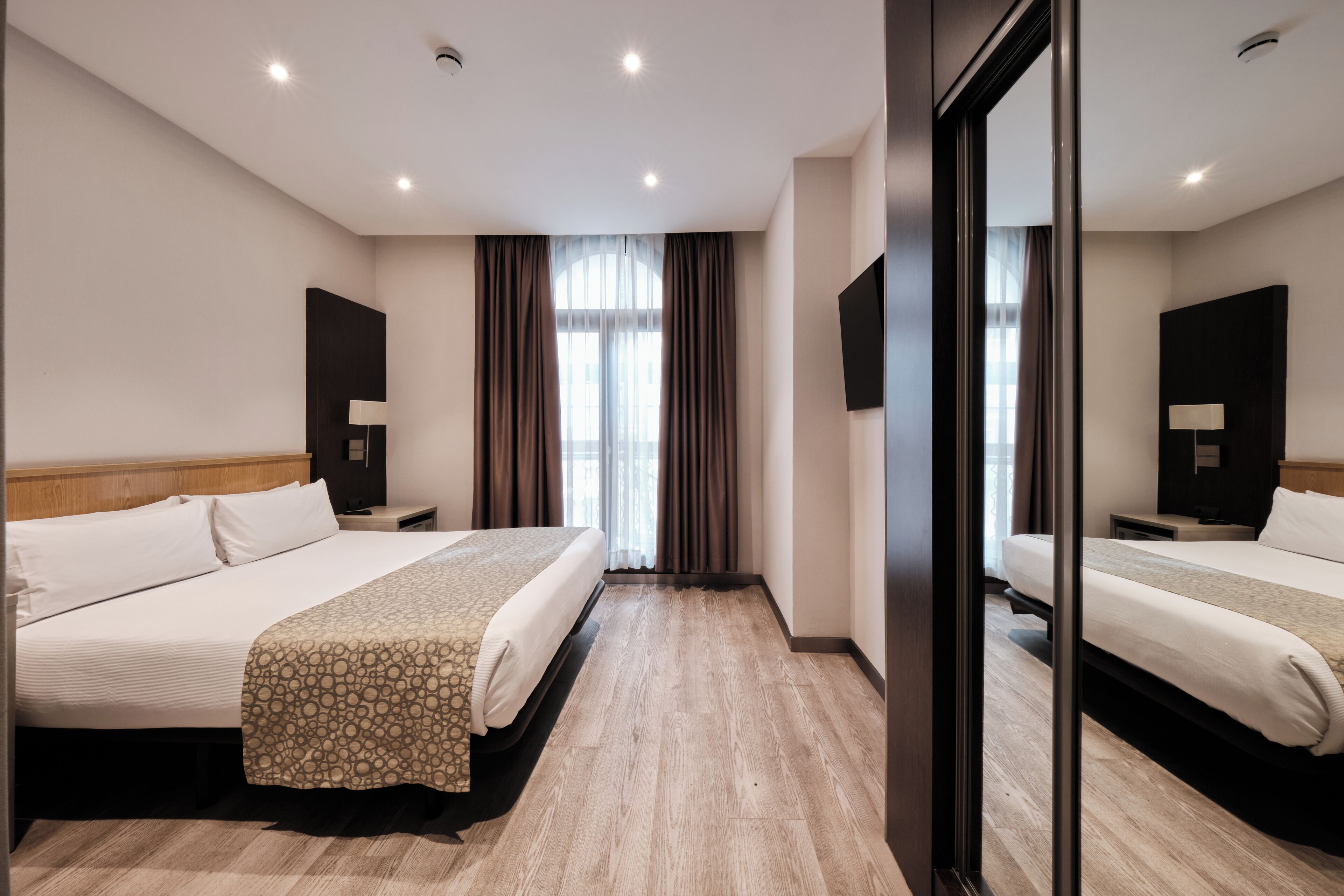 Una habitación de hotel con dos camas, un espejo grande y vistas a la ciudad desde la ventana.
