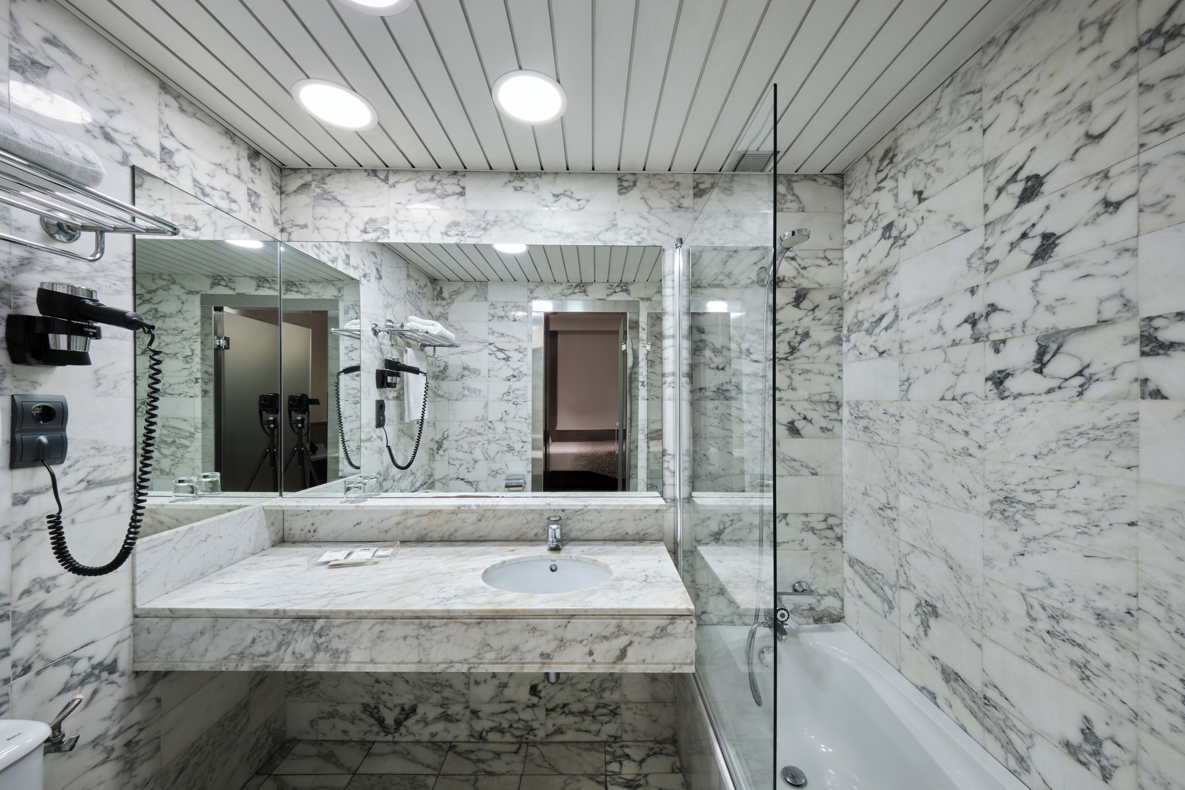 Ein modernes Badezimmer mit Marmorwaschbecken, einer Duschkabine aus Glas und einem großen Spiegel.