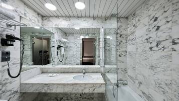 Un baño moderno con lavamanos de mármol, cabina de ducha con paredes de vidrio y un espejo grande.