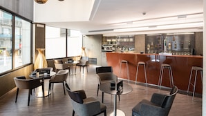A modern hotel lobby with a bar area, seating arrangements, and large windows offering views. - Catalonia Sagrada Familia (Barcelona)