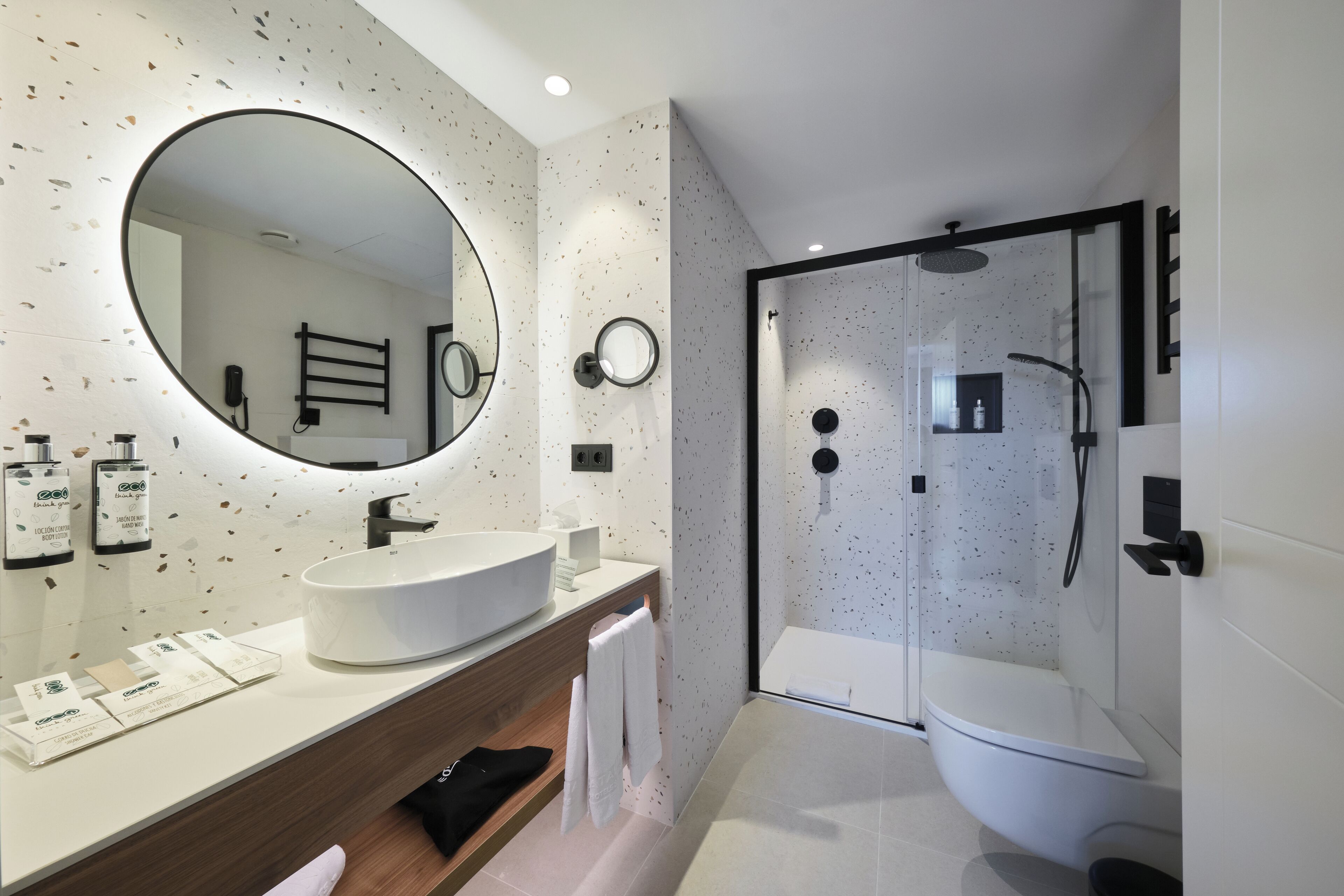 A modern bathroom with a large round mirror, a white sink, and a glass-enclosed shower.
