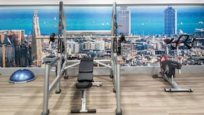 A gym with a cityscape view, including a large window, exercise equipment, and a blue exercise ball. - Catalonia Sagrada Familia (Barcelona)