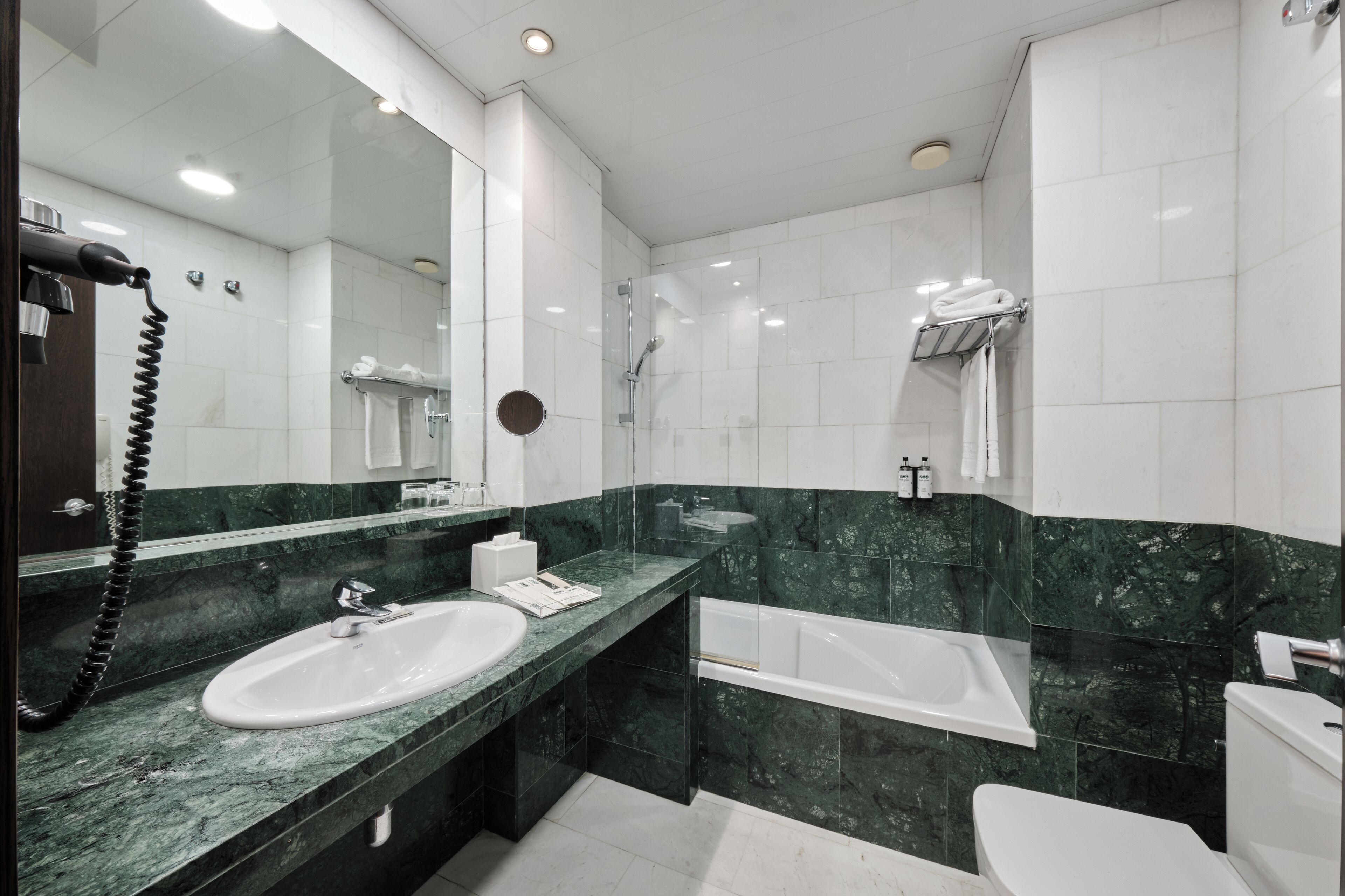 A modern bathroom with a large mirror, two sinks, a bathtub, and a toilet.