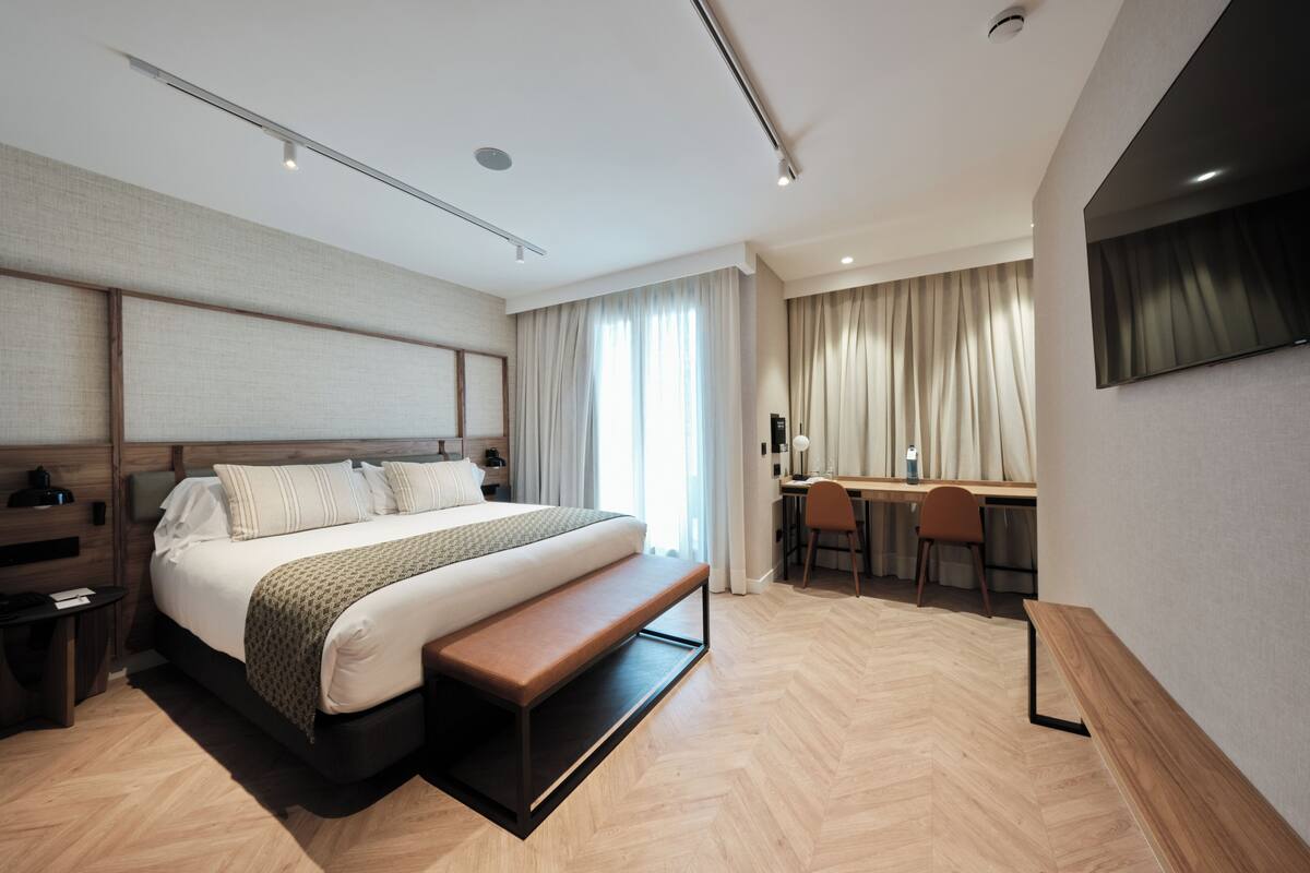 Quarto de hotel moderno com uma cama grande, uma mesa de escritório e uma TV fixada na parede.