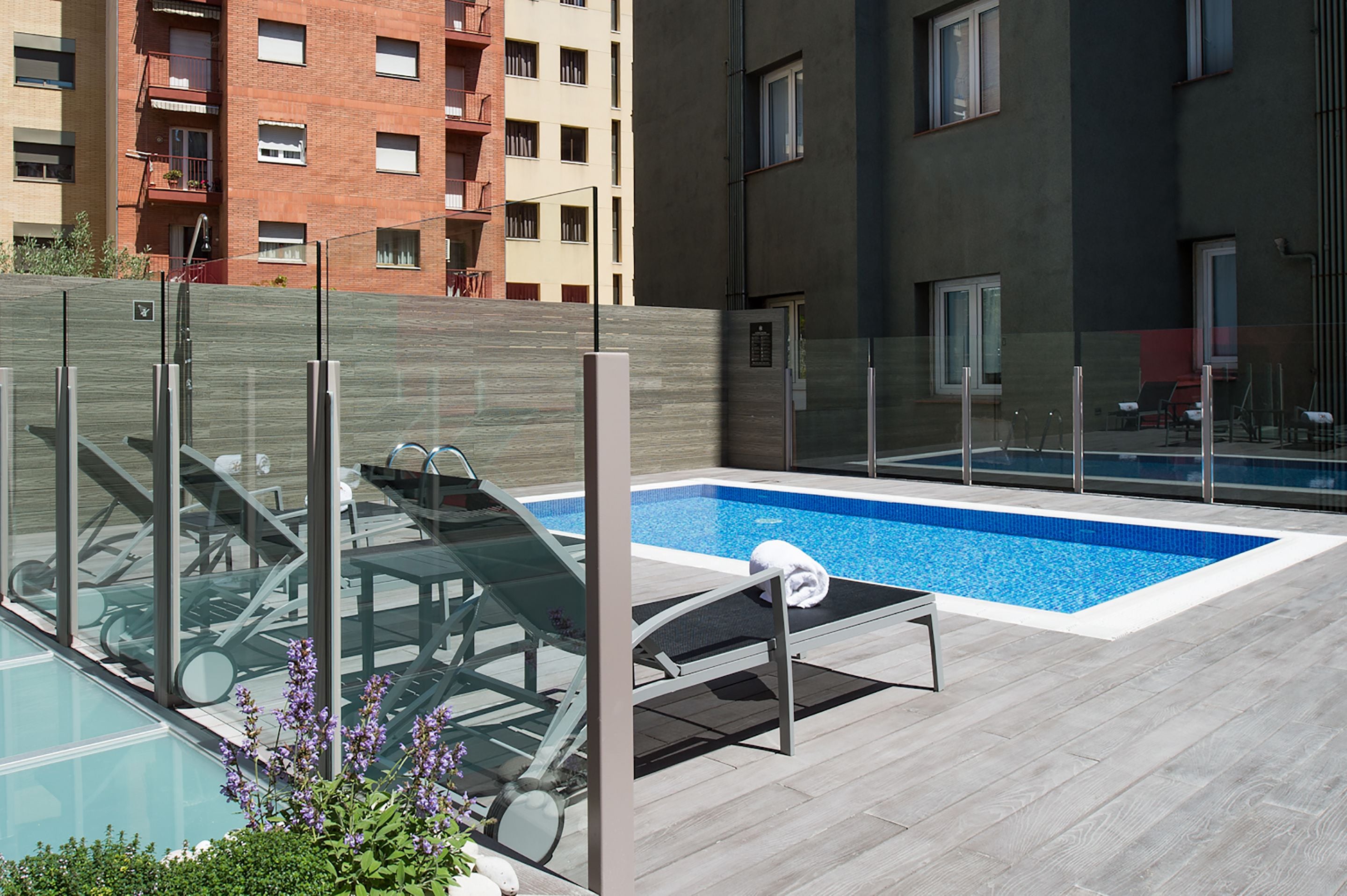 Zona de piscina al terrat amb baranes de vidre, gandules i una petita piscina.
