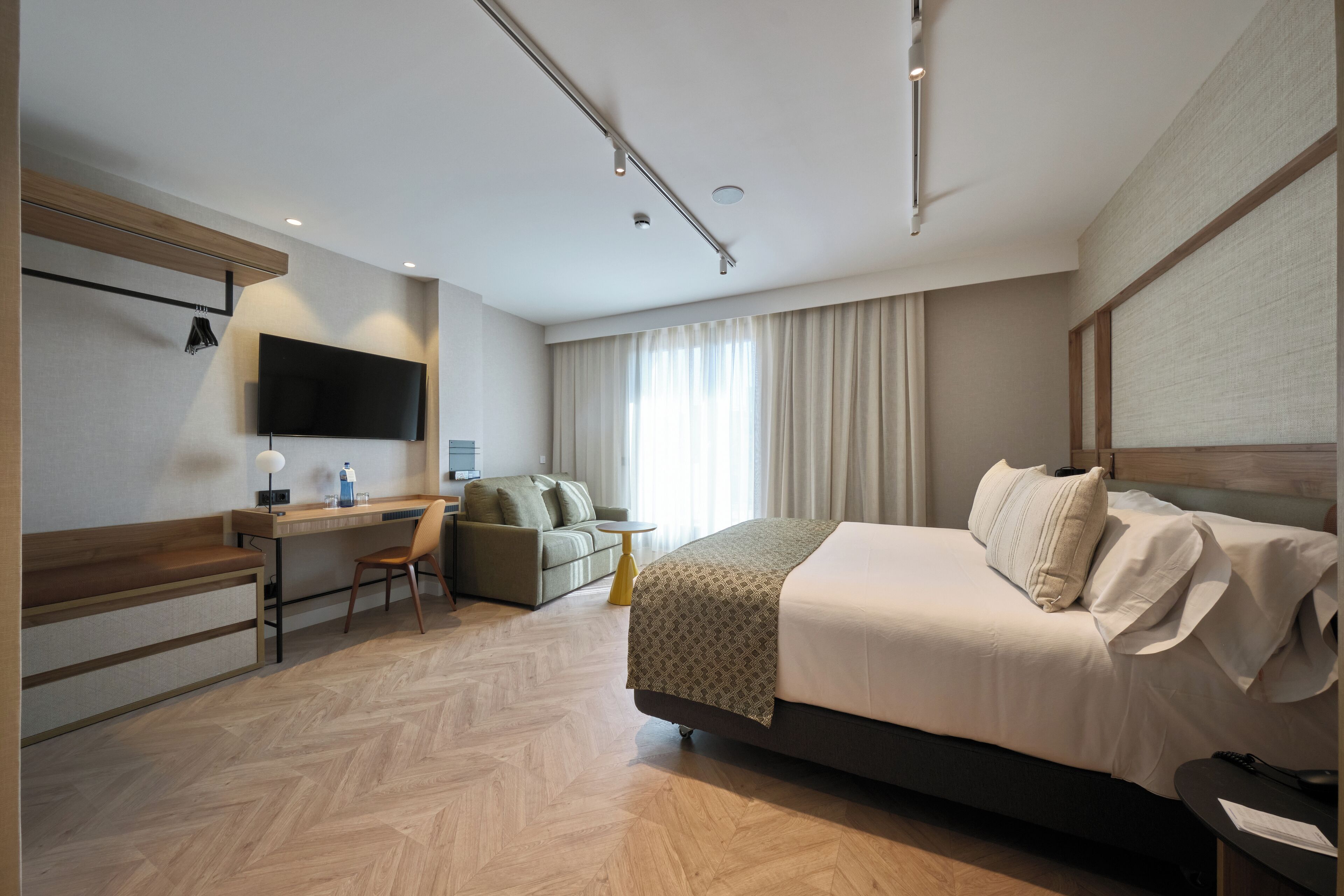 Une chambre d’hôtel moderne équipée d’un grand lit, d’un bureau, d’une chaise, d’une télévision et d’une fenêtre avec des rideaux.