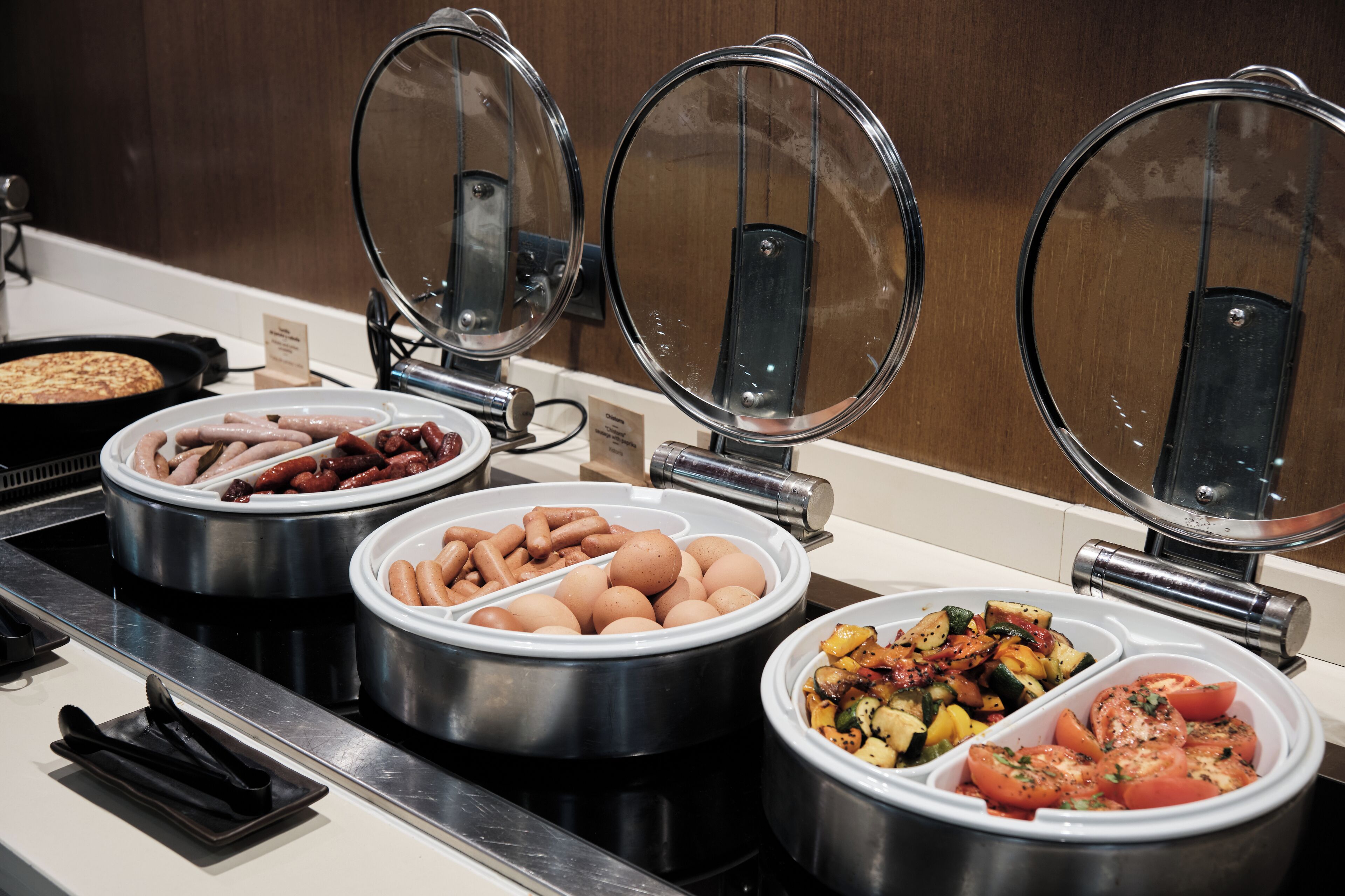 A buffet with various food items including sausages, eggs, and vegetables.