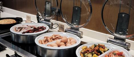 A buffet with various food items including sausages, eggs, and vegetables.