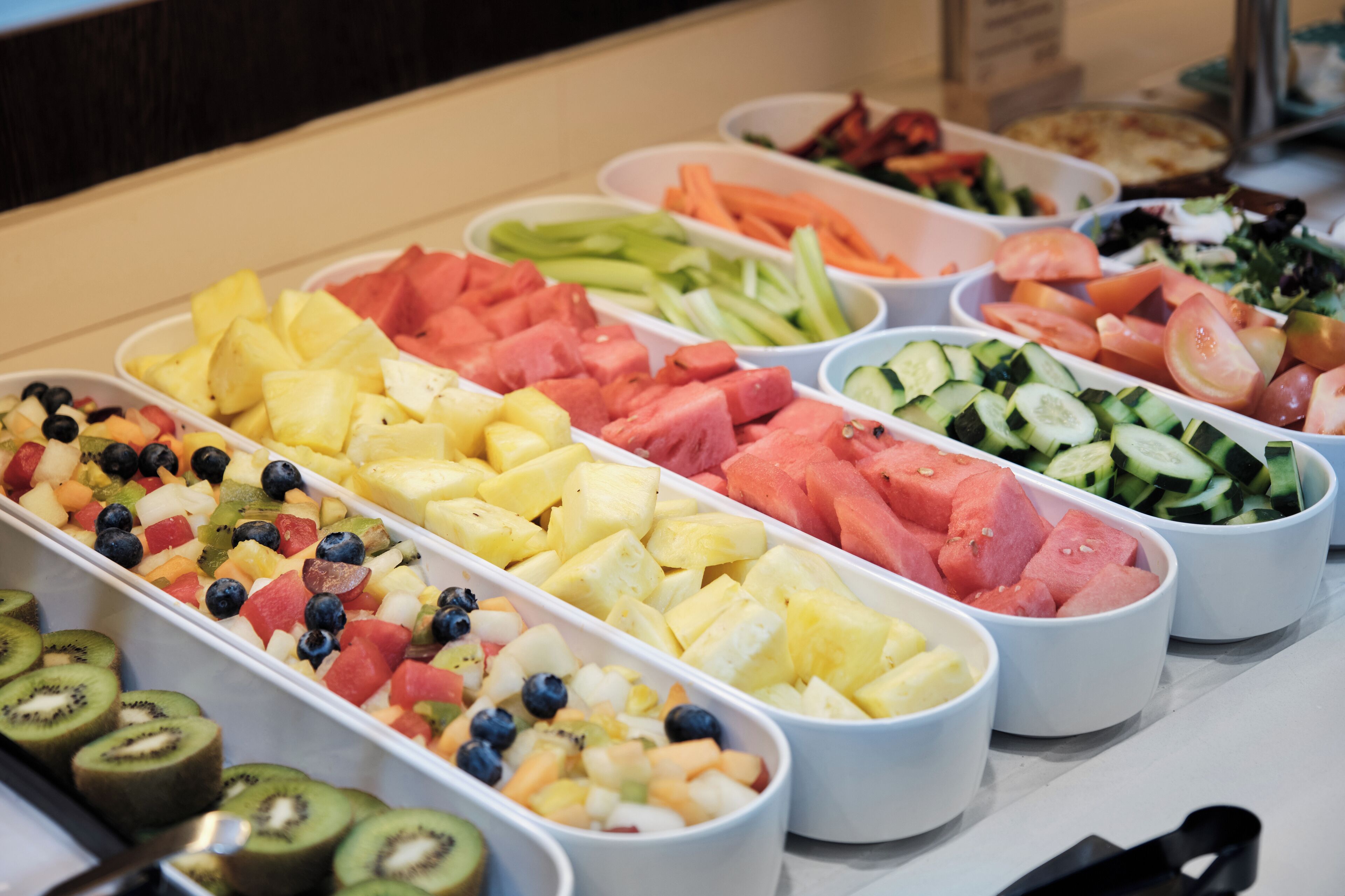 A buffet with various fruits and vegetables arranged in white trays.