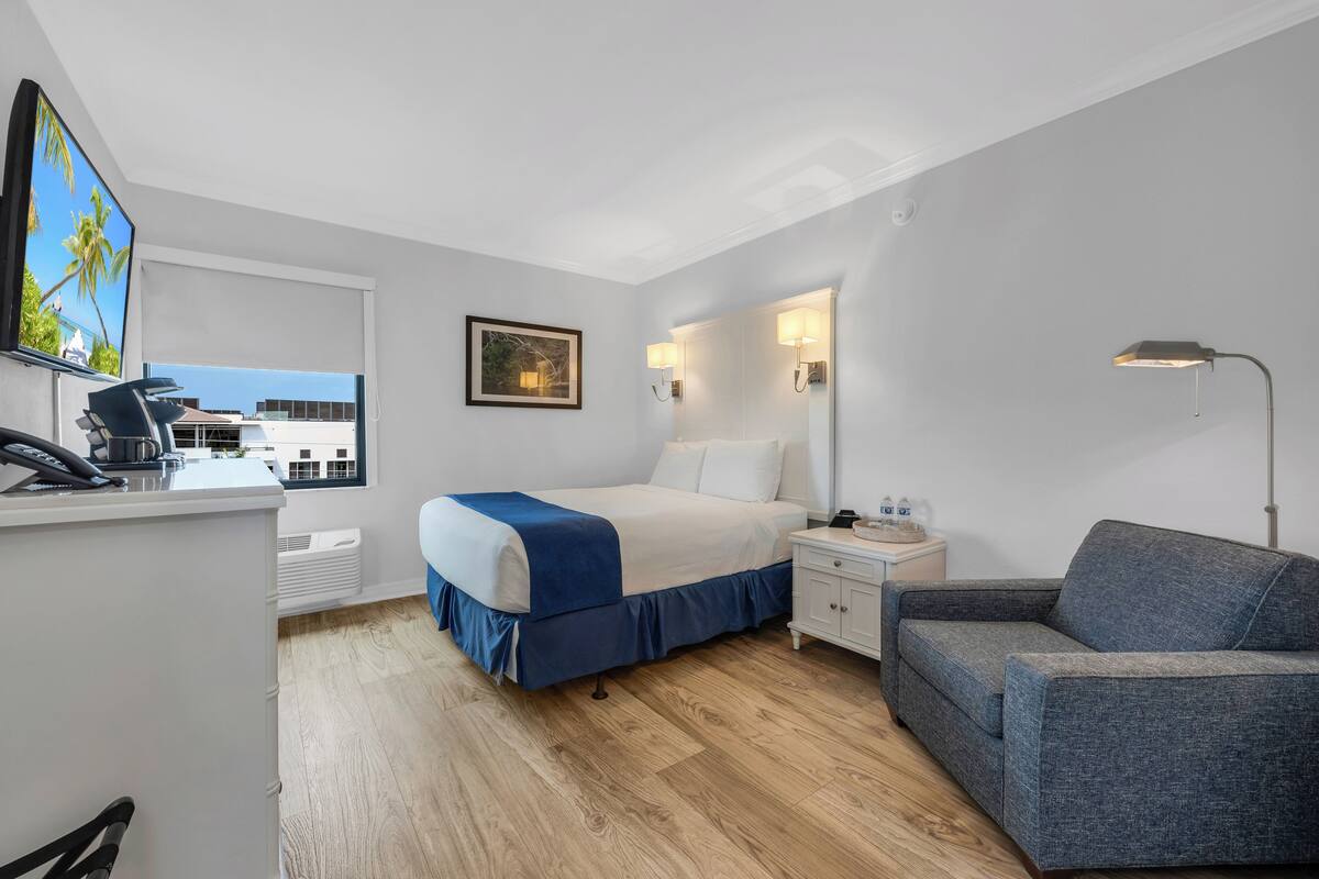 A hotel room with a bed, a desk with a phone, a chair, a sofa, a TV, and a window with a view.